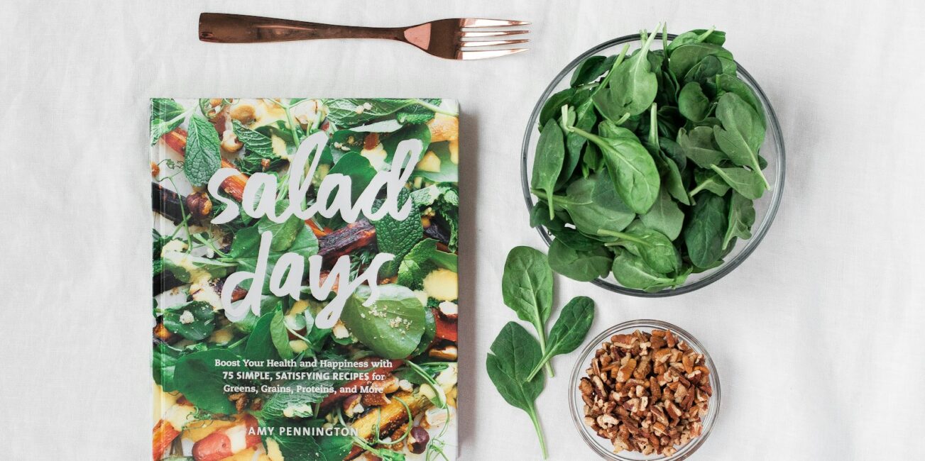 Salad day cookbook beside clear glass bowl with vegetable